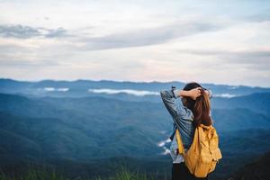 Happy young woman traveler relaxing and looking at the beautiful sunset on the top of mountain photo