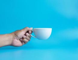 Man hand holding a white coffee cup, filled with hot black coffee americano, no sugar no milk, ready to drink, refreshing. aroma awake fresh to work placed on a blue isolated background photo