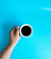 Man hand holding a white coffee cup, filled with hot black coffee americano, no sugar no milk, ready to drink, refreshing. aroma awake fresh to work placed on a blue isolated background photo