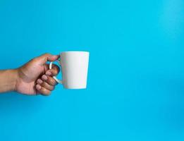 mano de hombre sosteniendo una taza de café con leche, llena de café negro caliente americano, sin azúcar ni leche, lista para beber, refrescante. aroma despierto fresco para trabajar colocado sobre un fondo azul aislado foto