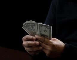 Computer and hands of a man wearing a black shirt, sitting on a chair and a table, is a thief, holding money, counting the amount obtained from hijacking or robbing, in a pitch-black room. photo