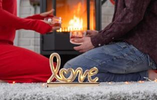 el hombre y la mujer enamorados en casa están sentados cerca de la estufa de la chimenea con un fuego ardiente en una alfombra acogedora. día de san valentín, pareja feliz, historia de amor, relaciones foto