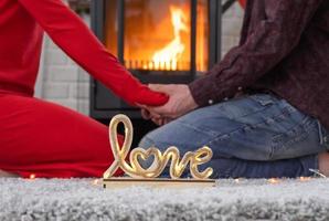 el hombre y la mujer enamorados en casa están sentados cerca de la estufa de la chimenea con un fuego ardiente en una alfombra acogedora. día de san valentín, pareja feliz, historia de amor, relaciones foto