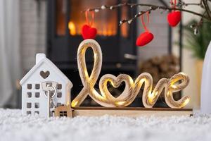Key to house with keychain against background of fireplace stove with fire and firewood in Valentine decor, love home. Moving to new house, mortgage, rent and purchase real estate photo