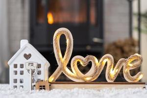 Key to house with keychain against background of fireplace stove with fire and firewood in Valentine decor, love home. Moving to new house, mortgage, rent and purchase real estate photo