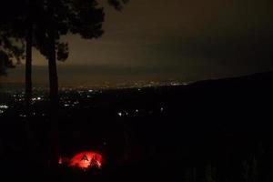 night in the forest. orange tent with light inside. city light view photo