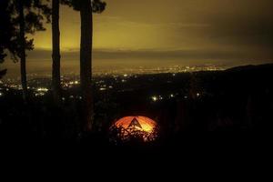 puesta de sol en la ciudad. vista de la luz de la ciudad desde la cima de la montaña. tienda de campaña en la noche oscura foto