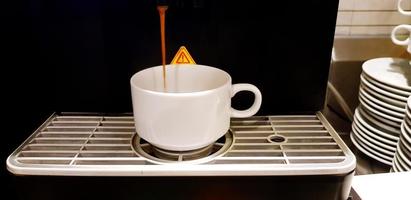 Close up hot coffee pouring from Fresh coffee maker machine in white cup. Refreshment drinking and Technology device concept photo