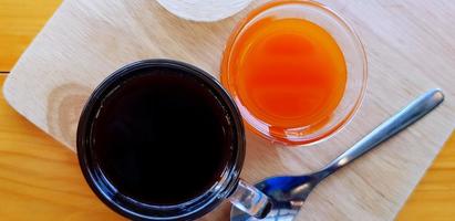 Top view of dark espresso shot with glass of orange juice and tea spoon on wooden tray for serving customer in morning at coffee cafe. Refreshment drinking concep photo