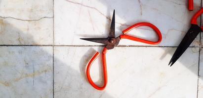 Two old red rusty scissors putting on white marble floor or background with copy space. Vintage object with sunlight shinning from beside photo