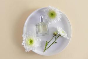 a glass bottle of perfume or spray lies on a ceramic plate among the white flowers of the chrysanthemum. pastel background. a place for a tecta. photo