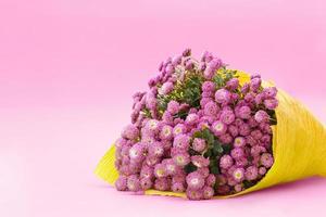 Bouquet of small lilac chrysanthemums in yellow paper on green background. Congratulation, birthday gift, international women's, mother's day. Copy space photo