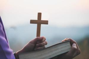 woman holding a holy bible and cross in her hands and praying  in the morning.  Hands folded in prayer on a Holy Bible in church concept for faith,   spirituality and religion. photo