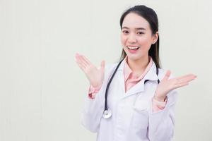 Beautiful young Asian woman doctor smiling cheerfully showing gestures in a medical gown photo