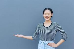 el retrato de una linda estudiante asiática tailandesa que se ve amistosa está de pie sonriendo alegremente y con confianza mostrando una comunicación tan buena como para presentar algo sobre un fondo gris. foto
