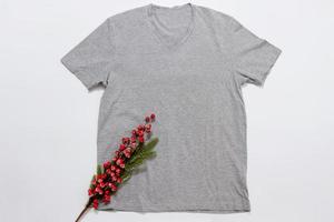 Close up grey blank template t shirt with copy space and Christmas Holiday concept. Top view mockup t-shirt and red holidays decorations on white background. Happy New Year accessories. Xmas outfit photo