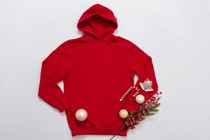 Close up red blank template hoodie copy space. Christmas Holiday concept. Top view mockup hoodie, scarf, hat. Red holidays decorations white background. Happy New Year accessories. Selective focus photo