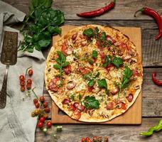 baked round pizza with smoked sausages, mushrooms, tomatoes, cheese and arugula leaves photo