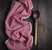 very old empty wooden spoon and red kitchen towel on a brown wooden background, photo