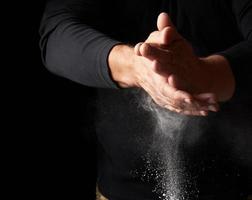 man claps his hands and scatters to the side a white substance on a black background photo