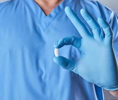 médico con guantes de látex azules sosteniendo una pastilla blanca foto