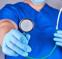 doctor in blue uniform and sterile gloves holding a medical stethoscope photo