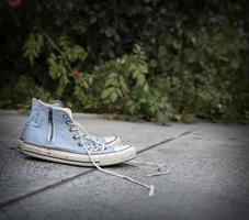 pair of old worn blue textile sneakers on gray asphalt photo
