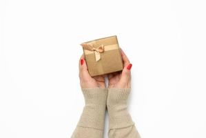 two female hands holding a square golden gift box with a bow on a white background, concept of gratitude photo