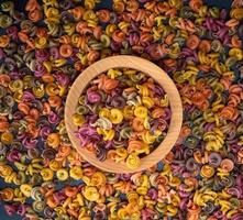 multicolored spiral raw pasta fusilli in a wooden bowl photo