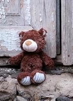 little teddy bear sits on the doorstep near an old door with cracked paint, photo