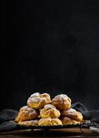 Baked eclairs with custard cream on a metal round plate sprinkled with powdered sugar photo