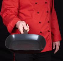 cook in red uniform holding an empty square black frying pan photo