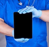 doctor in blue uniform and latex sterile gloves holding electronic tablet photo