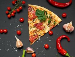 triangular piece of baked pizza with mushrooms, smoked sausages, tomatoes and cheese photo