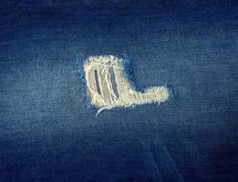 fragment of blue jeans fabric with a hole, full frame photo