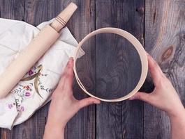 female hands holding a round wooden sieve for flour, next to an  wooden rolling pin photo