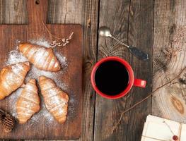 ceramic red cup with black coffee and wooden cutting board with baked croissants photo