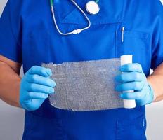 doctor in blue uniform and latex gloves holds a roll of white bandage for dressing gauze wounds photo
