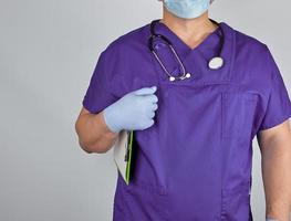 doctor in purple uniform and sterile latex gloves holds clipboard photo