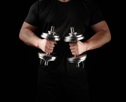 man in black clothes holds steel dumbbells in his hands, his muscles are tense photo