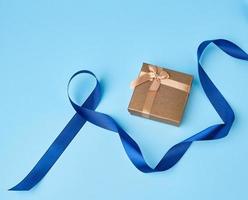 golden square box with a gift tied with a white ribbon with a bow photo