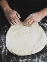 las manos de los hombres amasan una masa redonda para hacer pizza foto
