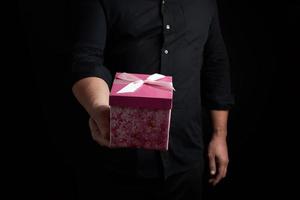 adult man in a black shirt holds a pink square box with a bow tied photo