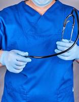 médico con uniforme azul y guantes de látex sosteniendo un estetoscopio negro foto