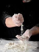 chef in black uniform sifts through his fingers white wheat flour photo