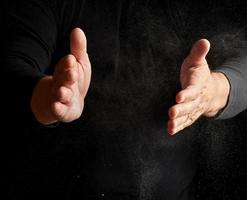 man claps his hands and scatters to the side a white substance on a black background photo