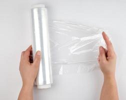 two hands hold a large roll of wound white transparent film for wrapping food photo