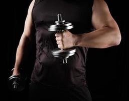 man in black clothes holds steel dumbbells in his hands photo