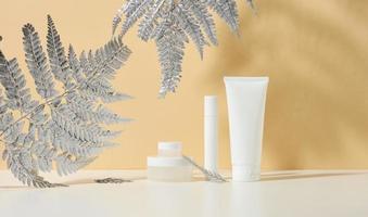 white tube for cosmetics, a jar of cream and silvery on a white table. Cosmetic on a beige shadow background. Cream bottle, lotion, cleanser, shampoo for skincare photo