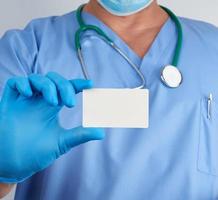 doctor in sterile latex gloves and blue uniform holds a blank white business card photo